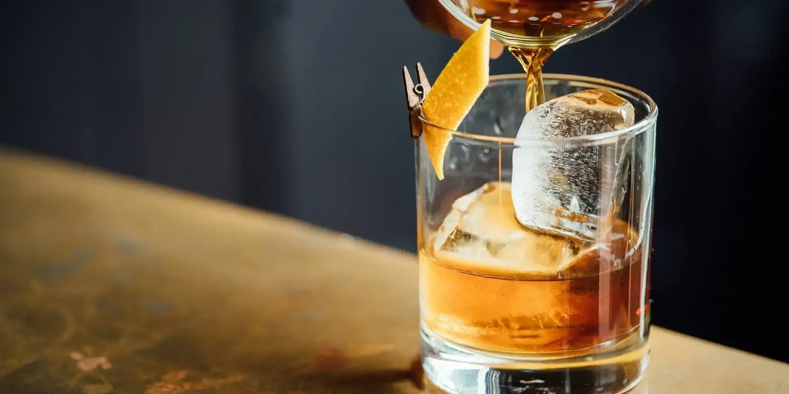 Cóctel colándose sobre un vaso con hielo en la barra de un bar