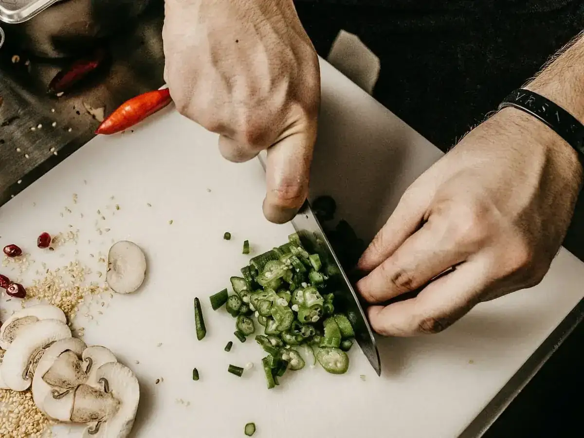 Manos cortando verduras con un cuchillo sobre una tabla en una cocina